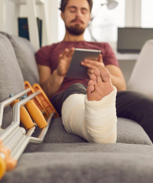 Image of a man sitting on the couch with an injured foot next to his crutches