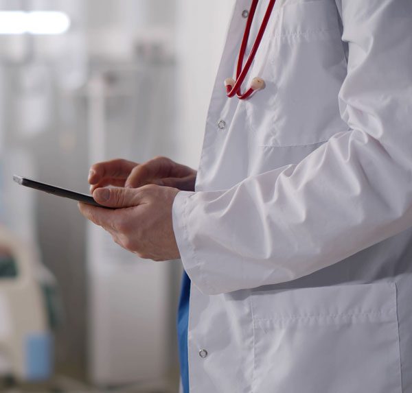 Image of a Doctor entering information on a tablet with a patient in the background